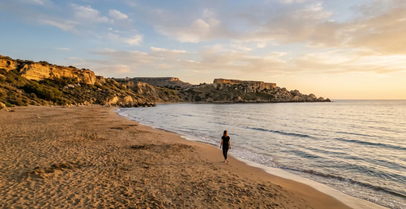 Une plage maltaise calme et déserte au coucher du soleil, avec une eau méditerranéenne paisible et des falaises de calcaire doré.