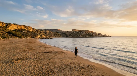 Une plage maltaise calme et déserte au coucher du soleil, avec une eau méditerranéenne paisible et des falaises de calcaire doré.